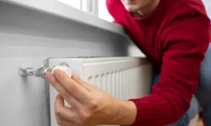 Mężczyzna w czerwonym swetrze reguluje zawór grzejnika, pokazując, jak odpowietrzyć grzejnik.