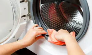 Ręce czyszczą gumową uszczelkę pralki pomarańczową ściereczką. Dbanie o czystość pralki to podstawa.