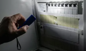 Ręka trzyma latarkę, oświetlając skrzynkę z bezpiecznikami. Brak prądu? Gdzie dzwonić, gdy wyłącznik główny jest włączony, a w domu ciemno?