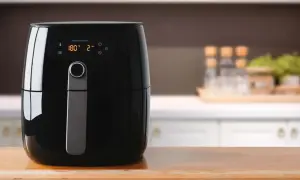 Czarny airfryer na drewnianym blacie. Cyfrowy wyświetlacz pokazuje 180°C i 2 minuty. Idealny do zdrowego gotowania, warto sprawdzić ranking airfryerów.