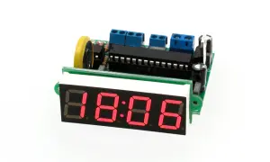 Elektroniczny zegar z czerwonym wyświetlaczem 18:06, zasilany przez płytkę drukowaną z elementami, w tym oscylatorem.