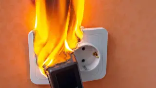 Gniazdko elektryczne w ogniu, prawdopodobnie z powodu zwarcia. Płomienie obejmują wtyczkę i część gniazdka.