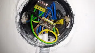 Widać przewody elektryczne w puszce, przygotowane do zerowania gniazdka. Żółto-zielony przewód uziemienia jest widoczny.