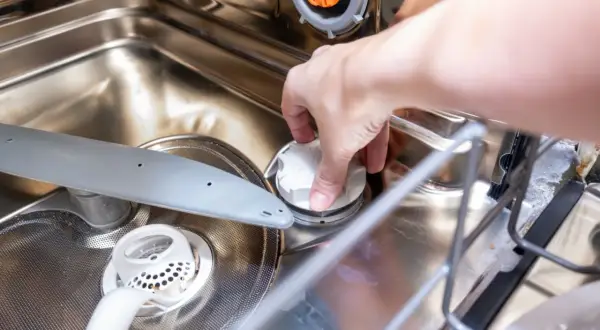 Dłoń odkręca białą nakrętkę, pokazując, gdzie wsypać sól do zmywarki.