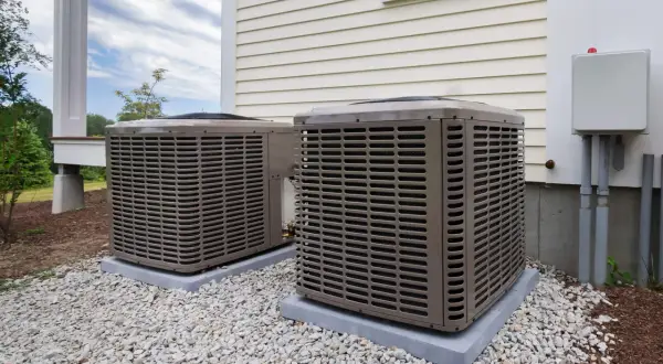 Dwa klimatyzatory przy nowoczesnym domu energooszczędnym, otoczone białym żwirem.