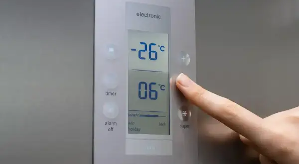 Palec naciska przycisk plus na panelu sterowania lodówki, regulując temperaturę. Na wyświetlaczu widać -26°C i 06°C.