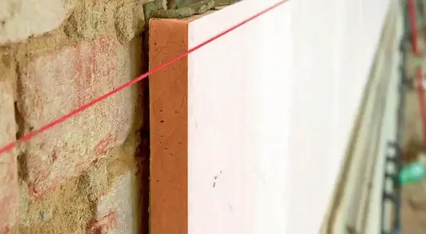 Poliuretan co to? Izolacja termiczna na ceglanym murze, wyznaczona czerwoną nicią.