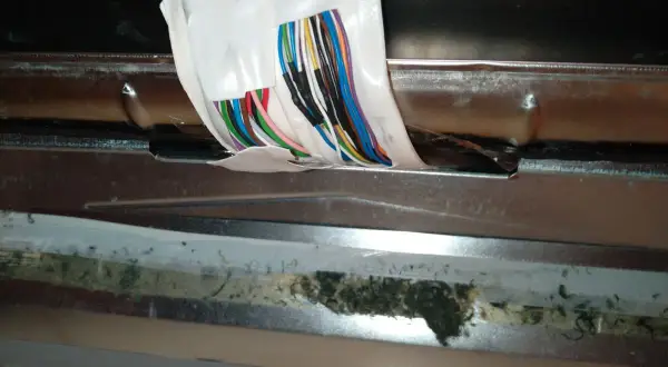Zmywarka Beko błąd E02: widoczne uszkodzone przewody i brud pod metalową osłoną.
