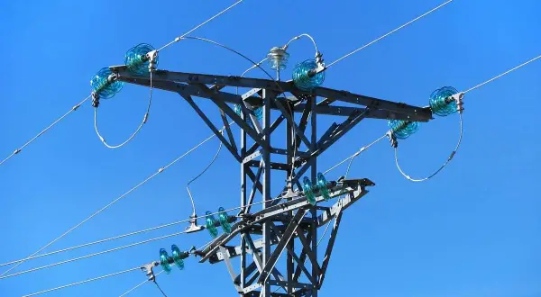 Metalowa konstrukcja słupa energetycznego z niebieskimi izolatorami, przez które biegnie linia średniego napięcia.