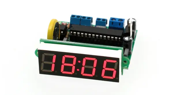 Elektroniczny zegar z czerwonym wyświetlaczem 18:06, zasilany przez płytkę drukowaną z elementami, w tym oscylatorem.