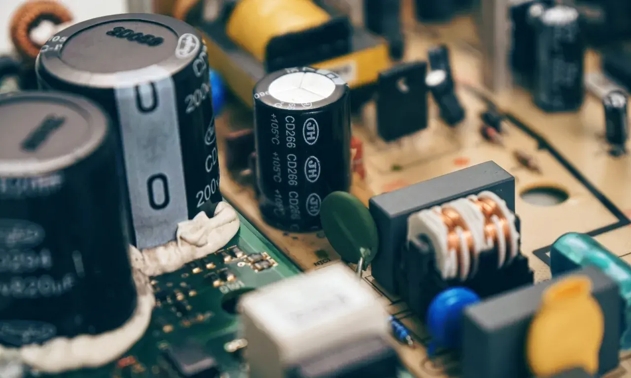 Zbliżenie na budowę kondensatora i innych elementów elektronicznych na płytce drukowanej.