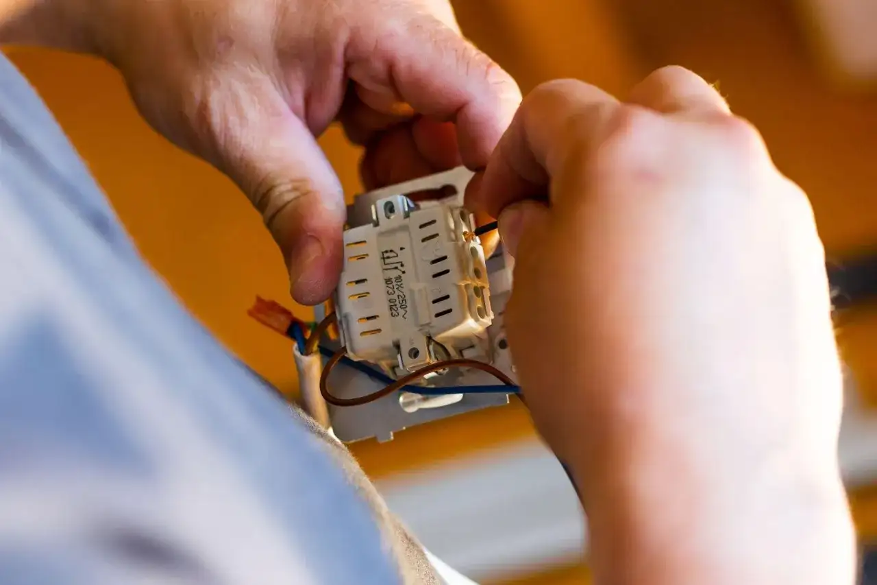 Ręce montują gniazdko elektryczne. Zastanawiasz się, ile za punkt elektryczny? To praca dla elektryka.