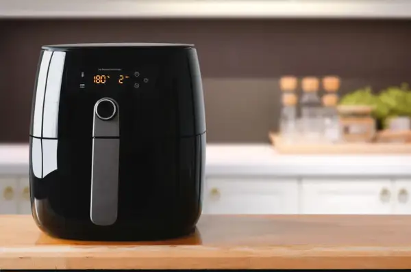 Czarny airfryer na drewnianym blacie. Cyfrowy wyświetlacz pokazuje 180°C i 2 minuty. Idealny do zdrowego gotowania, warto sprawdzić ranking airfryerów.