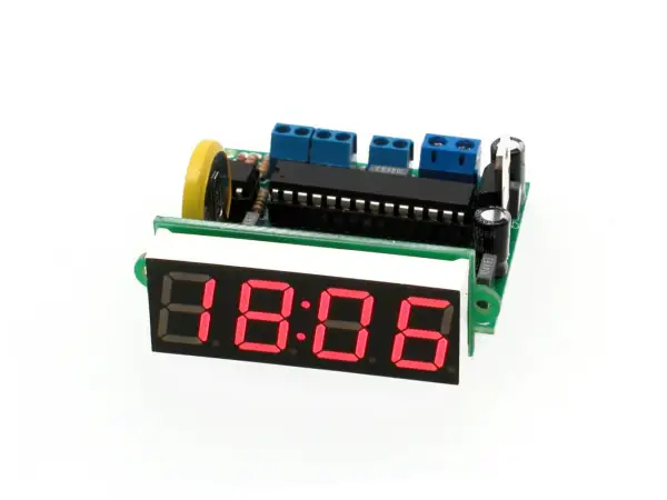 Elektroniczny zegar z czerwonym wyświetlaczem 18:06, zasilany przez płytkę drukowaną z elementami, w tym oscylatorem.
